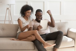 Excited happy african family couple looking at digital tablet feel winners overjoyed by lottery winning bet bid, celebrate good internet news, euphoric with great online victory prize new sale offer
