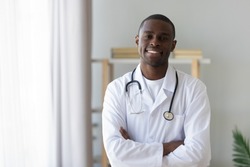 Smiling male african american professional young doctor stand arms crossed wear medical uniform looking at camera, happy confident black man general practitioner with stethoscope in office, portrait