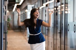 Excited funny young asian business woman celebrate success in victory dance, happy euphoric proud chinese female professional winner feel overjoyed by corporate reward standing in office corridor