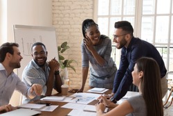 Happy friendly multiracial business team laughing working together at corporate briefing gathered at table, cheerful diverse office people group having fun talking enjoy teamwork during staff meeting