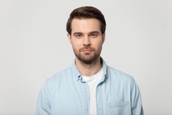 Close up head shot confident serious concentrated young man looking at camera studio portrait, isolated on grey white studio background. Thoughtful millennial guy posing for album photo.