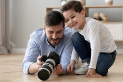 Dad holds photo camera explains teaches his little son how take photo create make art spend time together on warm floor, amateur or professional photographer share knowledge education of child concept