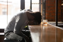 Depressed drunk young addicted man drinker sleeping alone on bar counter with whiskey glass, sad guy alcoholic passed out after drink too much alcohol addiction abuse, intoxication alcoholism concept