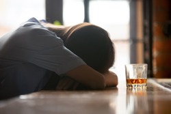 Drunk intoxicated woman sleeping on bar counter near whiskey glass in the morning, female heavy drinker alcoholic passed out lying asleep after booze, alcoholism problem, alcohol addiction concept