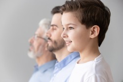 Happy intergenerational muti 3 three generation men family portrait, cute child boy son grandson looking forward think dream of future stand in row with young father and old grandfather, side view