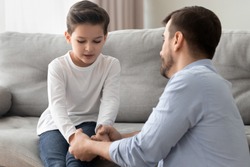 Worried loving young single father holding hand talking comforting upset little kid son sharing helping with problem, caring dad foster parent give support apologizing supporting listening child boy