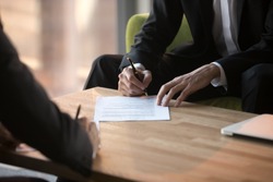 Close up businessmen signing partnership agreement, business partners making legal deal, putting signature on official paper document, taking loan or purchase property, male hands holding writing pen