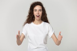 Astonished attractive millennial woman looking at camera, showing big size with both hands head shot portrait. Surprised shocked girl demonstrating huge measurement isolated on grey white background.
