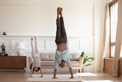 Full-length image african father and little daughter having fun fool around at home sportive active kid girl and dad do handstand position. Funny leisure activities, sporty healthy lifestyle concept