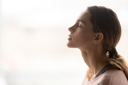 Serene young woman taking deep breath of fresh air relaxing meditating with eyes closed enjoying peace, calm girl tranquil face doing yoga pranayama exercise feel no stress free relief, side view
