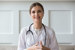 Head shot of woman wearing white coat stethoscope on shoulders looking at camera, doctor make video call interact through internet talk with patient provide help online counseling and therapy concept