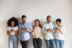 Happy diverse people using electronic devices, smartphones and tablet, standing in row on grey background, chatting in social network online, playing mobile phone games, having fun, shopping