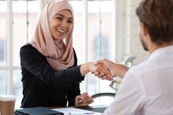 Happy asian muslim businesswoman hr manager employer wear hijab handshake hire male applicant make contract deal with partner collaborate shake client hand at job interview business meeting concept