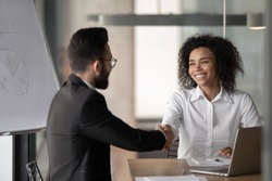 Happy millennial african American businesswoman shake hand greeting or get acquainted with male colleague, smiling biracial woman employee handshake man partner, closing deal at negotiations