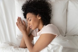 Beautiful African American woman with hands under cheek sleeping in comfortable bed top view, girl with closed eyes resting in bedroom, enjoying fresh bedclothes, lying on soft pillow close up