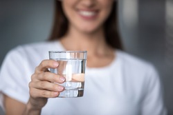 Smiling young lady holding fresh transparent pure filtered mineral water, happy healthy adult woman offering glass to camera as health care thirst hydration natural nutrition concept, close up view
