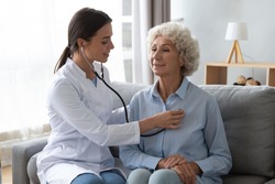 Young woman nurse doctor gp holding stethoscope examining old senior 60s grandma patient check heartbeat at homecare checkup medical visit at home hospital, older people cardiology healthcare concept