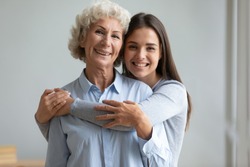 Beautiful adult daughter hug older mother at home, senior lady grandmother and young teen granddaughter embrace together, happy female two age generation family love care tenderness concept, portrait