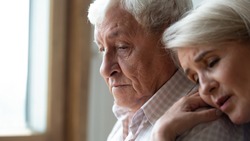 Worried middle aged woman embracing upset old man from back, side view head shot close up portrait. Sensitive mature wife showing support, comforting depressed elder husband, experiencing grief.