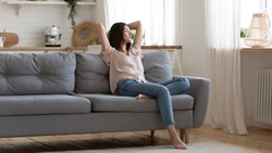 Serene lady housewife lounge sit on sofa feel fatigue napping hold hands behind head, calm young woman rest on comfort couch with eyes closed breath fresh air in cozy clean modern living room at home