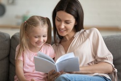 Caring single parent young adult mother and happy cute little preschool child daughter reading book learning education fairy tale story bonding enjoying family lifestyle hobby at home sit on sofa