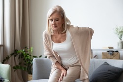 Elderly 60s woman got up from couch felt severe painful feelings in lumbar, massaging low back to reduce ache, suffer from backache discomfort, diseases of older people, sciatic nerve injury concept