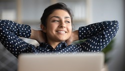 Happy satisfied indian woman rest at home office sit with laptop hold hands behind head, dreamy young lady relax finished work feel peace of mind look away dream think of future success concept