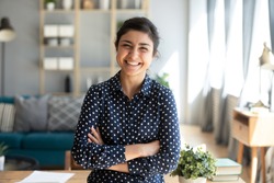 Smiling pretty young adult indian woman looking at camera posing at modern home arms crossed, cheerful happy ethnic girl student self employed lady laughing enjoying distance job education, portrait