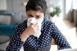Ill upset indian girl holding paper tissue blowing running nose sneezing in handkerchief got flu fever caught cold influenza sit at home, flue sinus virus disease symptom concept, face close up view