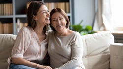 Happy senior mother and grownup daughter sit relax on couch in living room talk laugh and joke, smiling overjoyed middle-aged mom and adult girl child rest at home have fun enjoying weekend together
