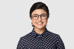 Head shot studio portrait millennial indial pretty smiling girl wearing eyeglasses, looking at camera. Confident student intern, young company worker, female professional isolated on grey background.