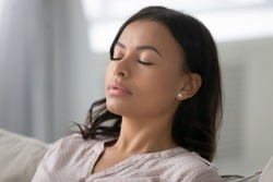 Close up of calm young African American woman rest on couch at home sleeping peacefully daydreaming, millennial female relax on sofa in living room, take nap, breathe fresh air, stress free concept