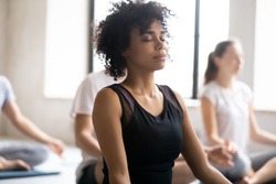 Yoga class concept, close up focus on mixed race African female closed eyes do meditation practice with associates during session. No stress, reducing fatigue after work out sport activity, wellness