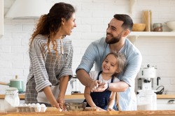 Overjoyed young family with little preschooler daughter have fun doing bakery in kitchen together, happy parents enjoy weekend with small girl child baking biscuits pastries, making pie at home