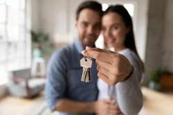 Focus on keys, held by excited young spouses homeowners. Happy married family couple celebrating moving in new house home , demonstrating keys, standing in apartment, real estate mortgage concept.