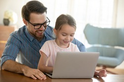 Head shot smiling young father in eyeglasses cuddling small preschool daughter, watching funny video on computer. Happy single dad shopping online on laptop with adorable little child girl at home.