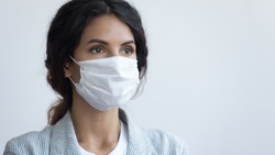 Young attractive serious woman in protective facial medical mask posing over blue background with copy space for text. Coronavirus COVID19 pandemic infection outbreak prevention, personal care concept