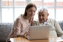 Grown-up daughter and old 80s father choose goods or services via internet or web surfing together at home. Younger generation caring about older relatives teaching using computer useful apps concept