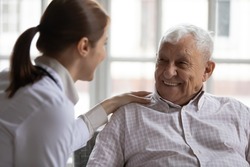 Caring geriatric nurse in white coat cares for grey-haired elderly man in nursing home, listen him relieve solitude, provide support help during visit at home. Homecare eldercare caregiving concept