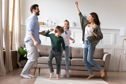 Full length overjoyed married couple dancing to favorite music in living room with adorable two children siblings. Excited happy kids son daughter having fun with energetic young parents at home.
