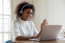 African tutor of language start on-line lesson with trainee wave hand smiling looks at pc screen. Mixed-race woman in headphones communicating distantly, e-learning process, application usage concept