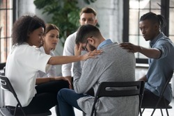 Diverse people supporting unhappy man at therapy session, touching shoulders, sitting in circle. Stressful businessman getting psychological help, trust and support, drug alcohol addiction treatment.