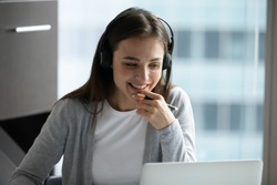 Happy millennial female in headphones watch webinar on laptop in modern office, smiling young businesswoman have fun laugh talk on video call with client or colleague use wireless Internet connection