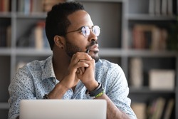 Pensive African American man in glasses distracted from computer work look in distance thinking or pondering, thoughtful biracial male lost in thoughts make plans visualizing, business vision concept