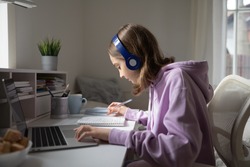 Teen girl school pupil wearing headphones studying online from home making notes. Teenage student distance learning on laptop doing homework, watching listening video lesson. Remote education concept