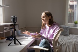 Teen girl blogger influencer recording video blog concept speaking looking at smartphone on tripod at home table. Teenager social media vlogger shooting vlog, streaming online podcast on mobile phone.