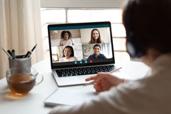 Woman sitting at desk noting writing information studying at home with multiracial students diverse ladies makes video call using video conference application, view over girl shoulder to laptop screen