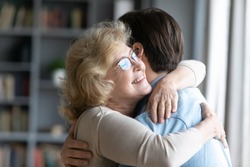 Loving elderly mother in glasses closed eyes enjoy moment strong cuddles adult son after long separation, grandmother glad to see grandson multi generational family reunion, love and bonding concept