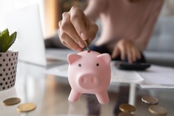 Close up young female putting coin in piggy bank. Woman saving money for household payments, utility bills, calculating monthly family budgets, making investments or strategy for personal savings.