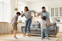 Full length overjoyed family of four jumping to music in modern studio living room. Excited young married couple dancing with playful little children siblings, spending active free time at home.